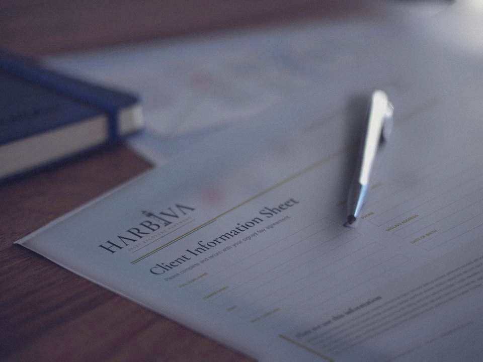 A Harbiva client information sheet on a wooden desk with a pen and a navy notebook