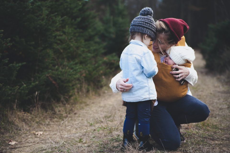 A mother kneeling outdoors and hugging her young child